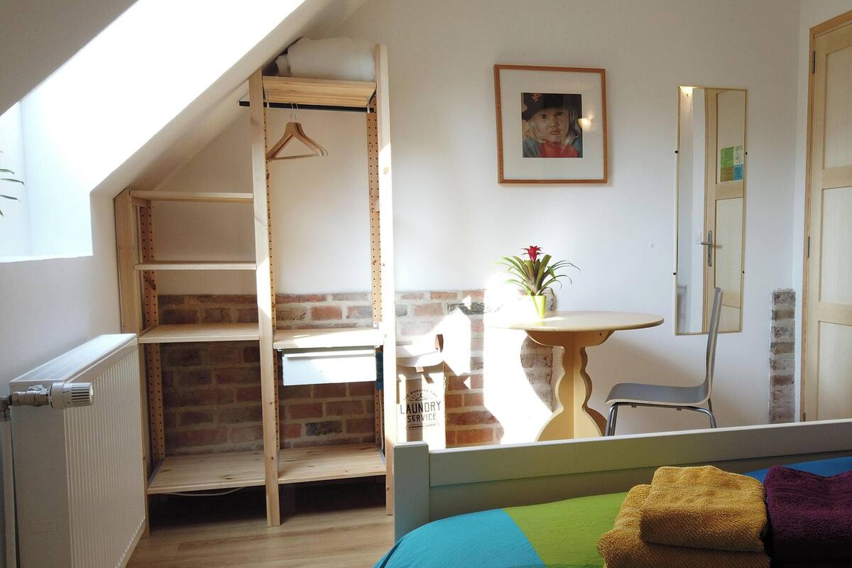 Une chambre à coucher avec un lit, un fauteuil suspendu, une petite table avec une plante, un miroir et une porte avec une pancarte.