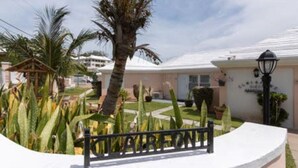 A hotel with a white exterior, palm trees, and a well-maintained garden. - Clairfont, Jobson's Cove / Warwick Long Bay/ Horseshoe Beach -  APARTMENT 1 (Warwick)
