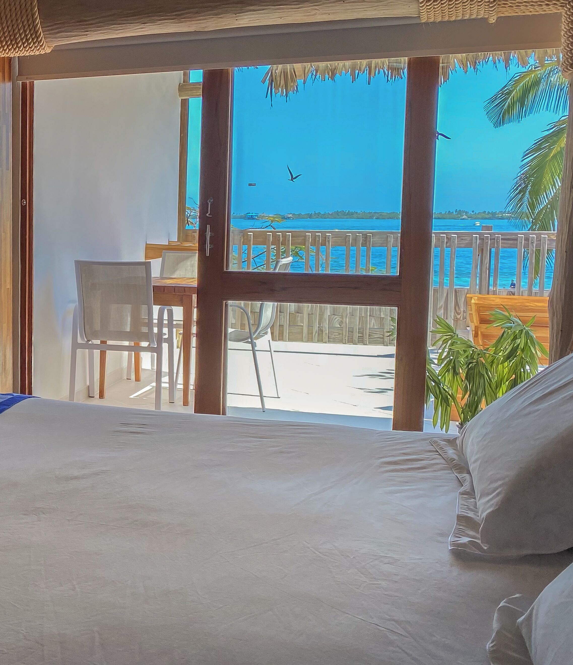 A room with a bed, a wooden desk, and a view of the beach and ocean.
