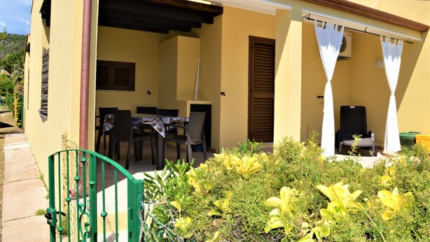 En gul bygning med en overdækket terrasse, et bord med stole og en stol under en hvid markise.