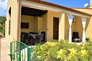 A yellow building with a covered patio, a table with chairs, and a chair under a white awning.