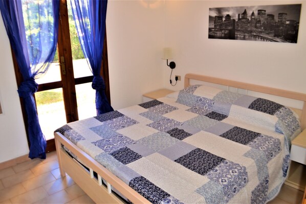 A bedroom with a wooden bed, a nightstand, a wall-mounted lamp, and a cityscape picture.