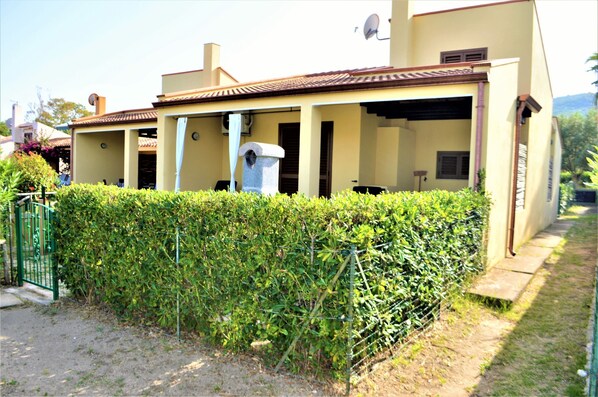 A two-story house with a covered patio, a satellite dish, and a small garden area. - Bilocale Riccardo (Muravera)
