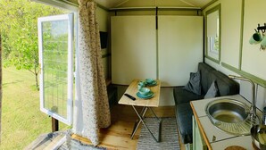 A compact room with a wooden table, a sofa, a sink, and a window with curtains. - Hillcrest Hut (Kilgetty)