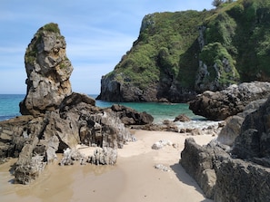 Uma praia rochosa com águas turquesa cristalinas e uma grande formação rochosa.