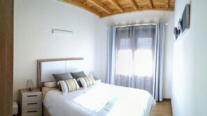 A bedroom with a wooden ceiling, a bed with multiple pillows, a nightstand, and a window with curtains. - MODERN APARTMENT IN PECHÓN (Pechón)