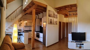 A modern kitchen with wooden beams, a dining area with a sofa, and a TV on a stand. - MODERN APARTMENT IN PECHÓN (Pechón)