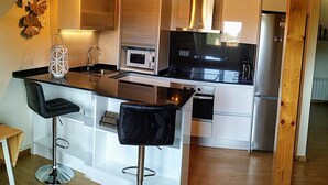 A modern kitchen with a central island, bar stools, stainless steel appliances, and a wooden ceiling. - MODERN APARTMENT IN PECHÓN (Pechón)