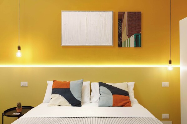 A neatly arranged bedroom with a bed, pillows, a nightstand, and a wall-mounted artwork.