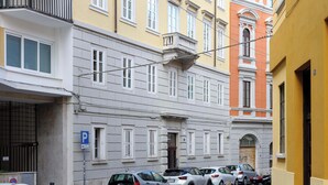 A row of parked cars along a narrow street with a building featuring a classic architectural style with white and yellow facades, a visible parking sign, and a balcony. - Brand New Guest room in the City Center★Free Wifi (Trieste)