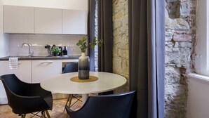 A modern kitchen with white cabinets, a black chair, a round table with a vase, and a stone wall. - Romantic Studio in the heart of Trieste ★Free Wifi (Trieste)