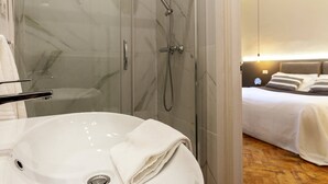 A modern bathroom with a glass-enclosed shower, a white sink, and a neatly made bed with a headboard. - Romantic Studio in the heart of Trieste ★Free Wifi (Trieste)