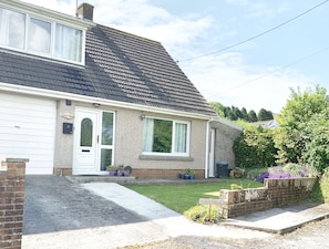 Une maison à deux étages avec une porte de garage blanche, un porche orné de plantes en pot et un chemin de briques menant à l’entrée.