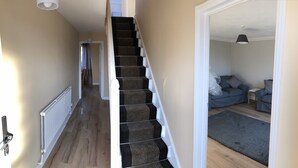 A staircase leading to a living area with a grey sofa and a small table. - Little Mead (Tenby)