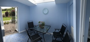 A small room with a glass table and four chairs, a potted plant, and a round mirror on the wall. - Little Mead (Tenby)