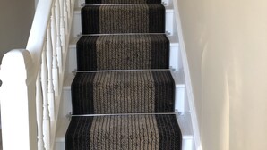 A staircase with a carpeted handrail and white balusters. - Little Mead (Tenby)