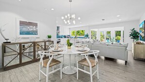 A modern kitchen with white cabinets, a dining area with white chairs, and a grey sofa.