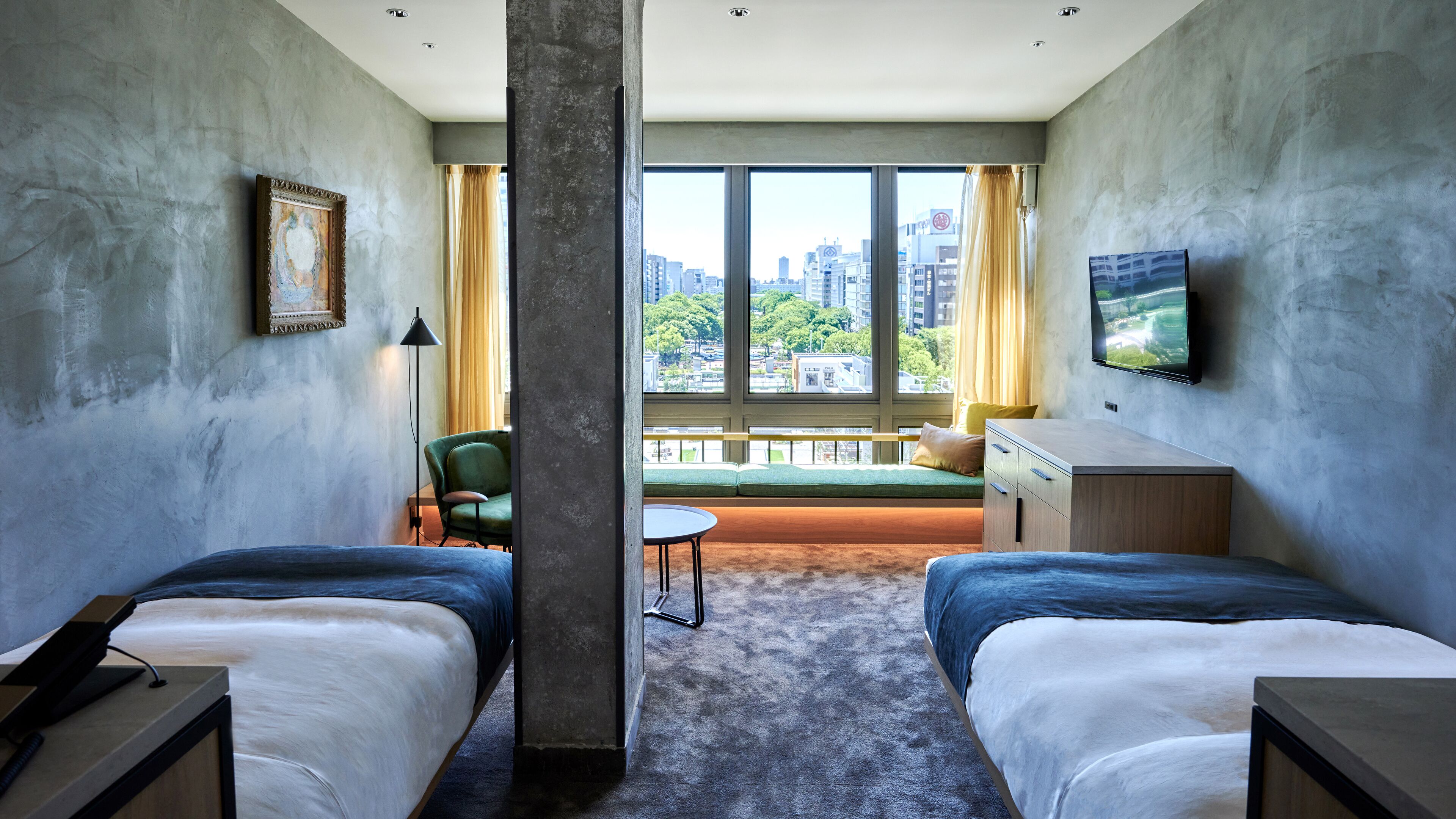 A hotel room with two beds, a sofa, a TV, a painting, and a view of the city.
