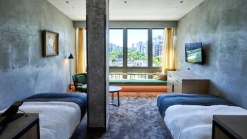 A hotel room with two beds, a sofa, a TV, a painting, and a view of the city.