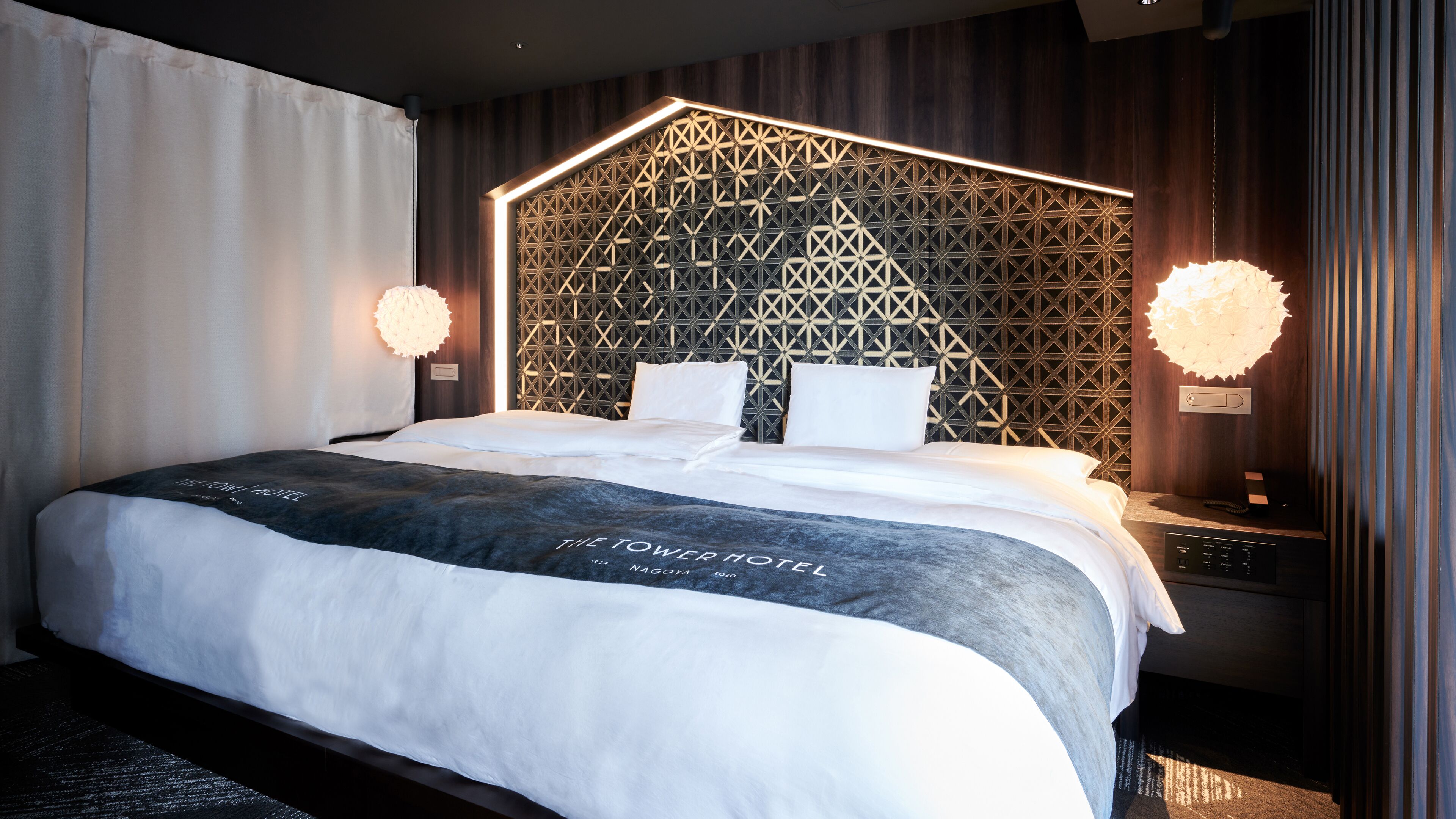 A modern hotel room with a geometric-patterned headboard, a large bed with white linens, and two bedside lamps.