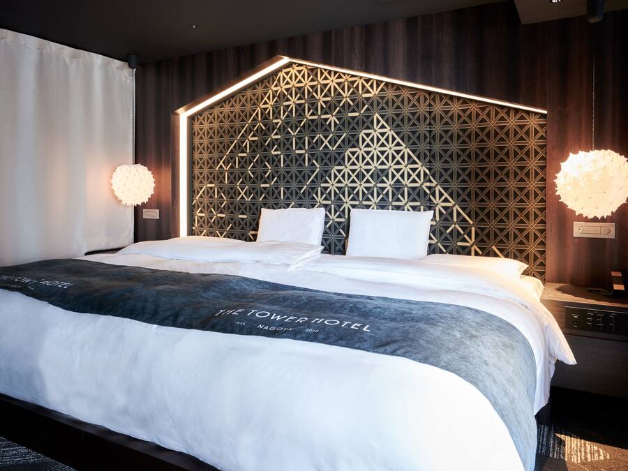 A modern hotel room with a geometric-patterned headboard, a large bed with white linens, and two bedside lamps.