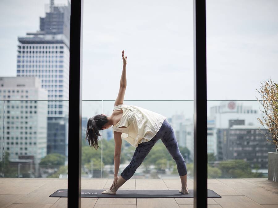 A person performing a yoga pose on a mat in an indoor setting with a cityscape view through large windows.