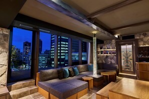 A modern living room with a large window offering a city view, a cozy sectional sofa, and a small wooden table. - The Tower Hotel Nagoya (Nagoya)