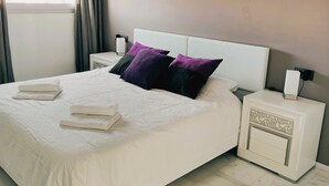 A modern bedroom with a large bed, white bedding, and a nightstand with a lamp. - Fine apartment by the sea, beach, nice and quiet yet close to Center (Villajoyosa)