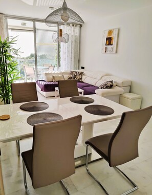 Uma sala de estar moderna com um sofá branco, uma mesa de jantar com cadeiras e uma janela grande com cortinas.