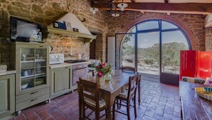Una cocina rústica con paredes de piedra, vigas de madera y un amplio ventanal de arco que da a un jardín.