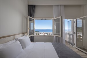 Habitación de hotel con una cama grande, vista al mar y un balcón con barandilla.