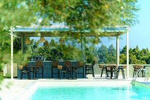 Zona de bar junto a la piscina con asientos exteriores y vistas a la piscina.