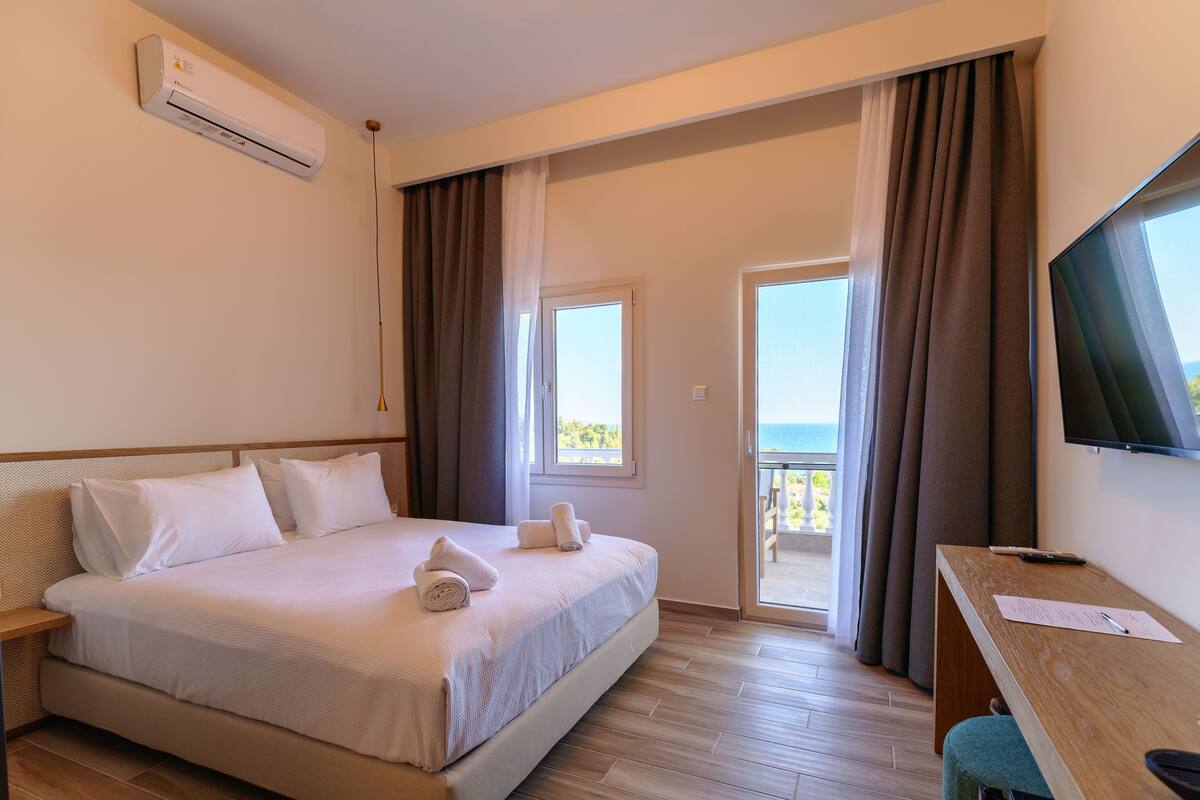 Une chambre d’hôtel avec un lit, un bureau, une télévision et un balcon avec des rideaux.
