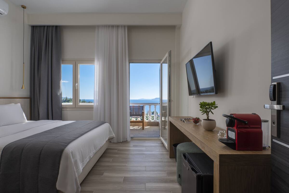 Une chambre d’hôtel avec un lit, un bureau sur lequel se trouve une machine à café rouge, une télévision et une vue sur la mer.