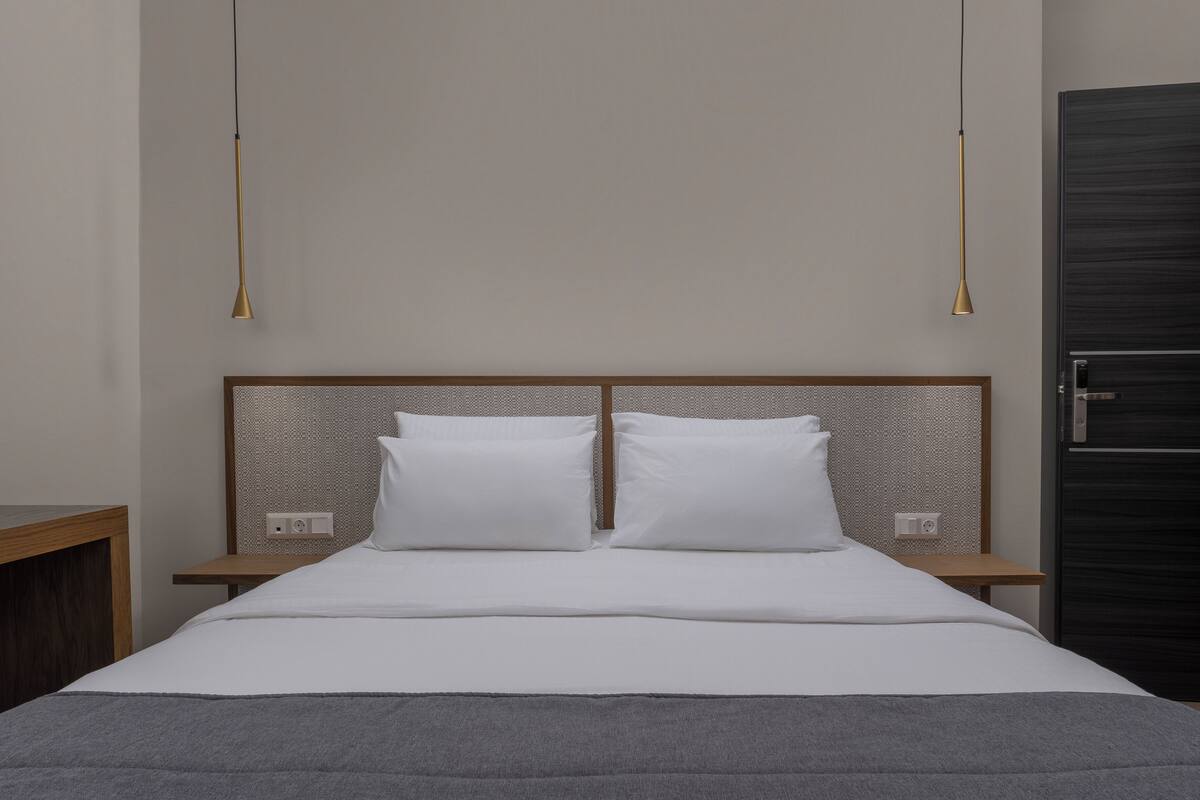 Un lit bien fait, avec du linge de lit blanc, deux tables de chevet et une armoire en bois foncé.