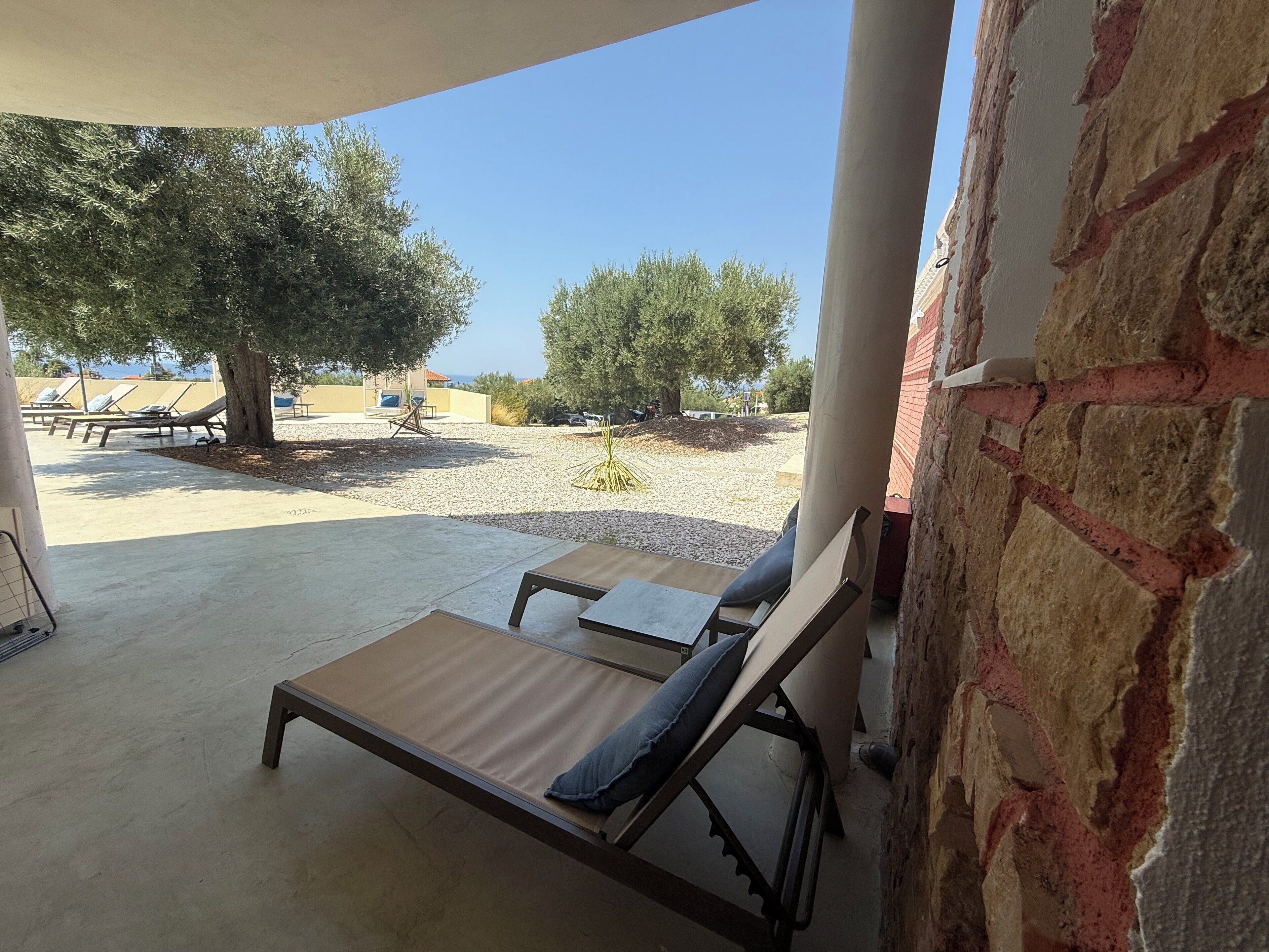 A covered outdoor area with lounge chairs and a view of a building and trees.
