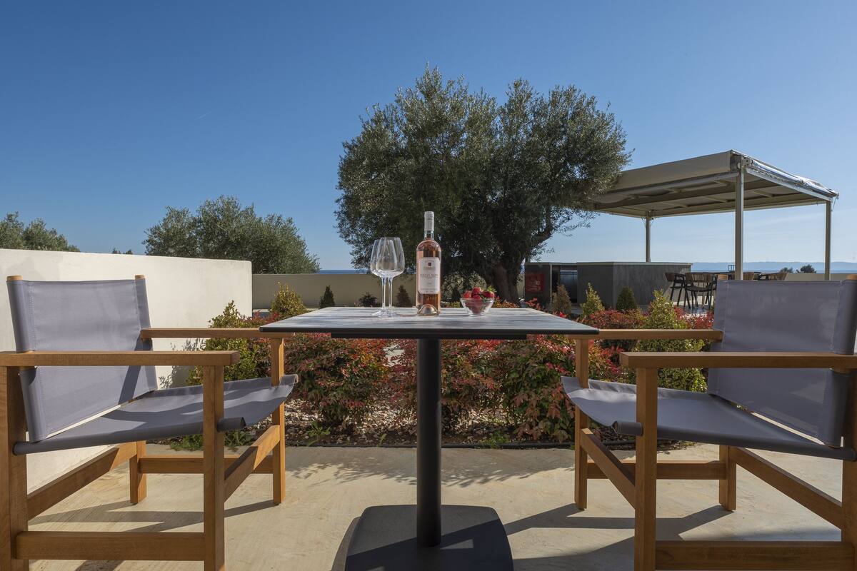 Une terrasse extérieure avec une table, deux chaises, une bouteille de vin et un verre.