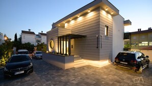A modern two-story house with a driveway, parked cars, and a well-lit entrance.