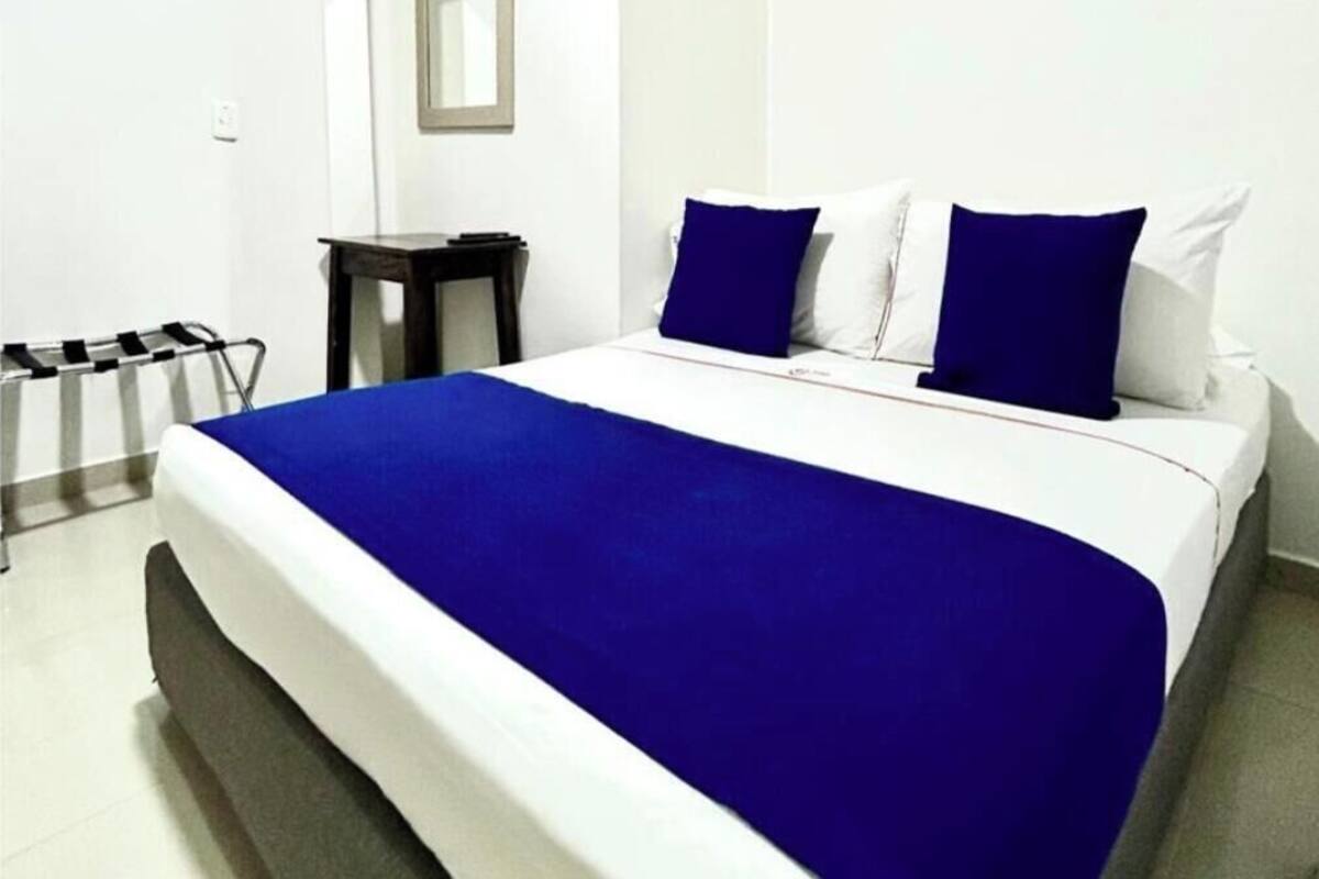 Una cama con una colcha azul, almohadas blancas y una mesita de noche.