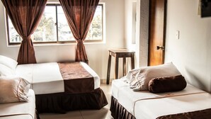 Una habitación de hotel con dos camas, un taburete de madera pequeño y una ventana con cortinas.