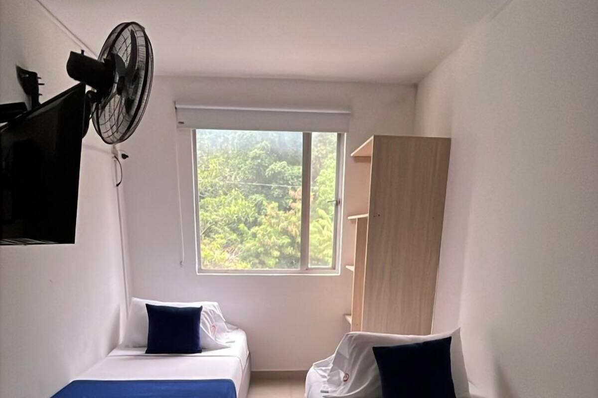 Una habitación con dos camas, una ventana con vistas, un ventilador de techo y un televisor montado en la pared.