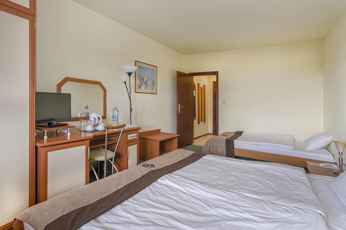 Een hotelkamer met een bed, een bureau met een computer, een stoel, een spiegel en een deur naar een andere kamer.