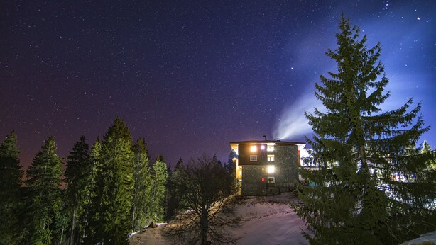 Uma cabana sob um céu estrelado, rodeada por árvores perenes e neve.
