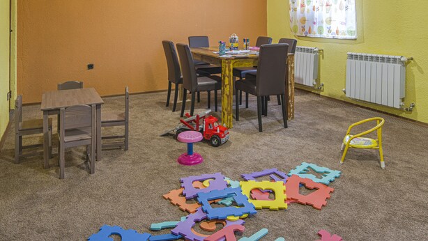 Een eetgedeelte met een tafel, stoelen, een radiator en een raam met gordijnen.