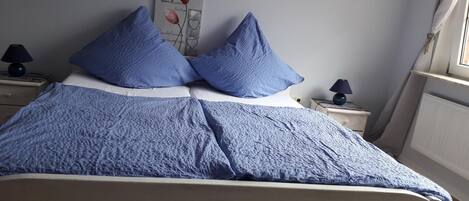 Ein Bett mit blauer Decke und Kissen, ein Nachttisch mit Lampe sowie eine Wand mit einem 'LOVE'-Schild und einer Blumenillustration.