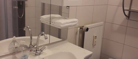 A bathroom with a sink, mirror, towel rack, and shower.