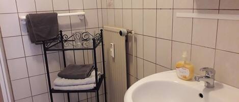 A bathroom with a white sink, a towel rack with two towels, and a bottle of hand soap.