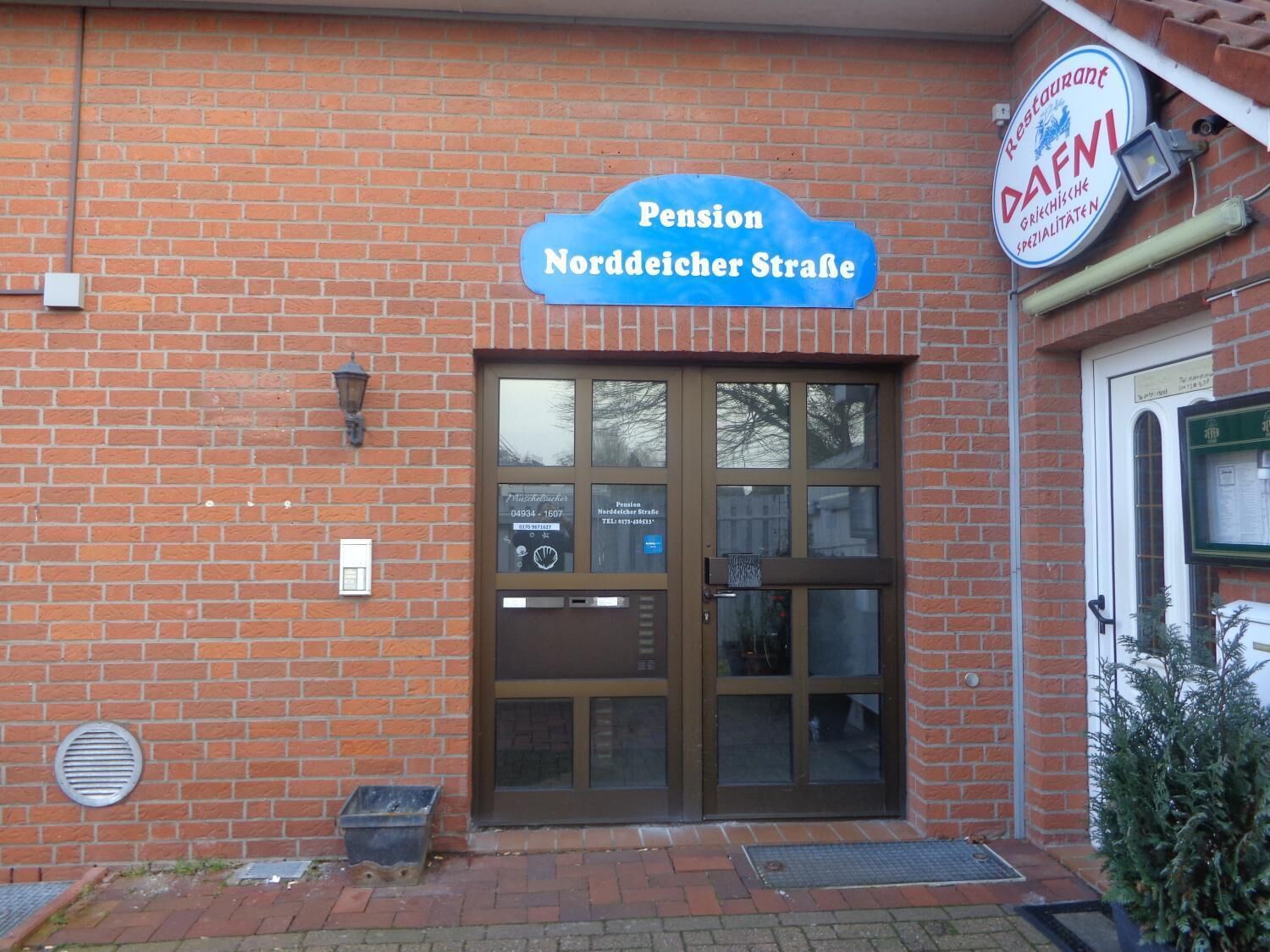 A building with a sign reading "Pension Norddeicher Straße" and a restaurant sign "DAFNI" above the entrance.