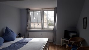 A bedroom with a bed, a window, a television, and a chair. - Pension Norddeicher Straße (Norden)