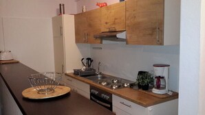 A kitchen with wooden cabinets, a stove, a sink, and a coffee maker. - Pension Norddeicher Straße (Norden)